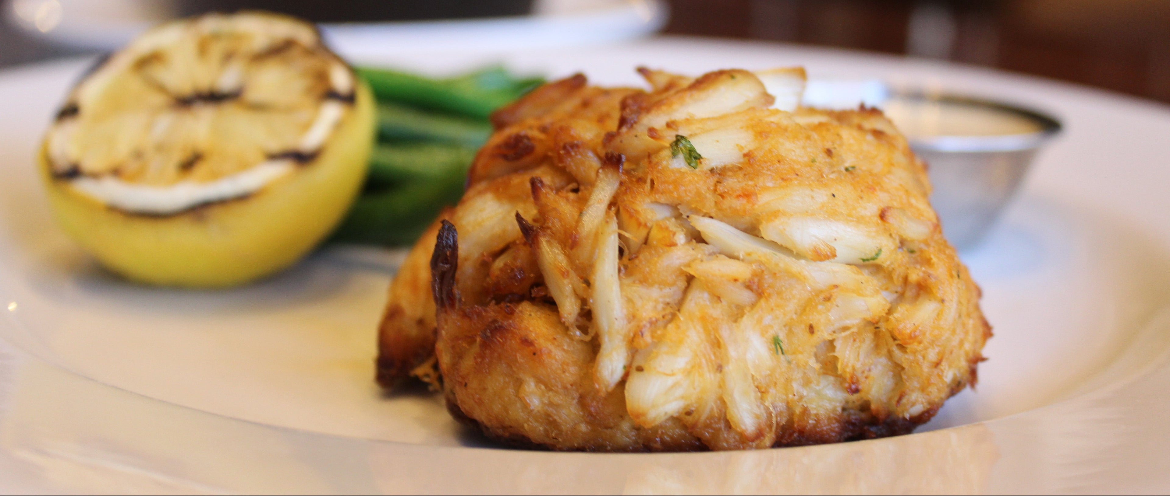 Crab Cake on plate accompanied by lemon, tartar sauce and sides